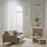 Beige sofa with gray pillows, white curtains, and a light earthy patterned rug, set against a soft gray wall.