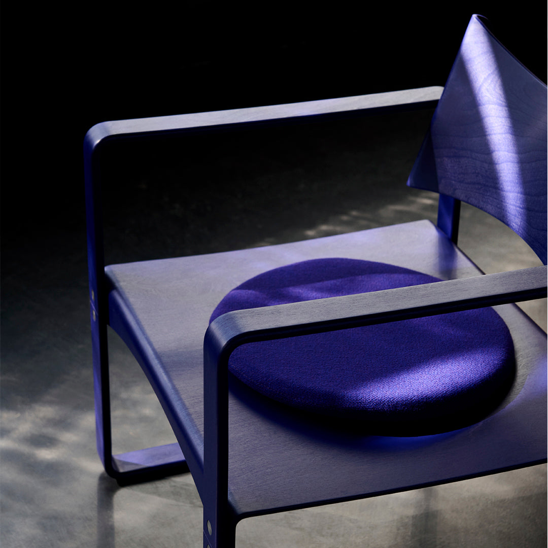 Modern chair featuring deep purple fabric and sleek geometric patterns, with a contrasting circular cushion.