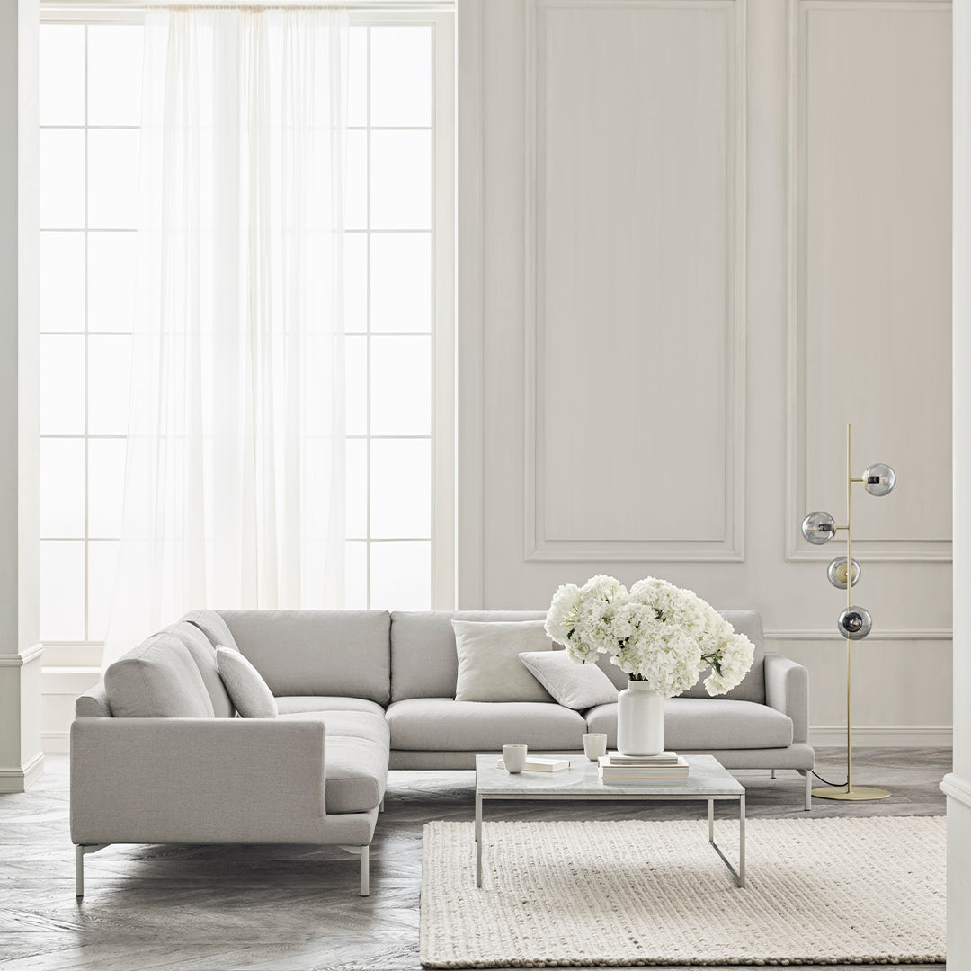 Light gray sectional sofa with clean lines, paired with a textured cream rug and white floral arrangement.