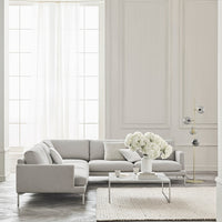 Light gray sectional sofa with clean lines, paired with a textured cream rug and white floral arrangement.