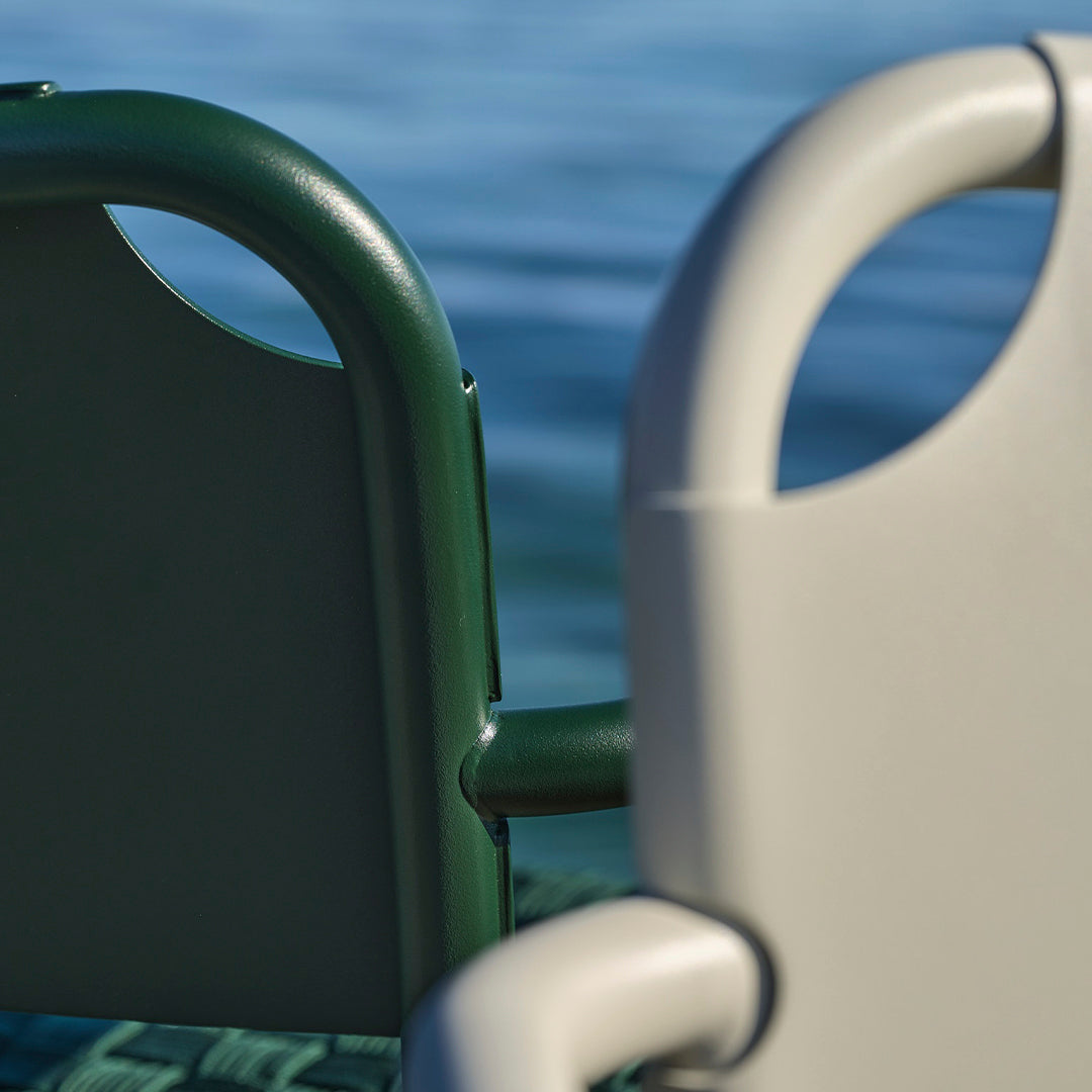 Green and gray outdoor chairs with smooth, rounded armrests against a water backdrop.