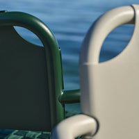 Green and gray outdoor chairs with sleek, minimalist design against a tranquil water background.