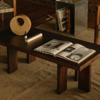 Dark wood coffee table with a smooth finish, beige decor accents, and a textured area rug in a warm, neutral palette.