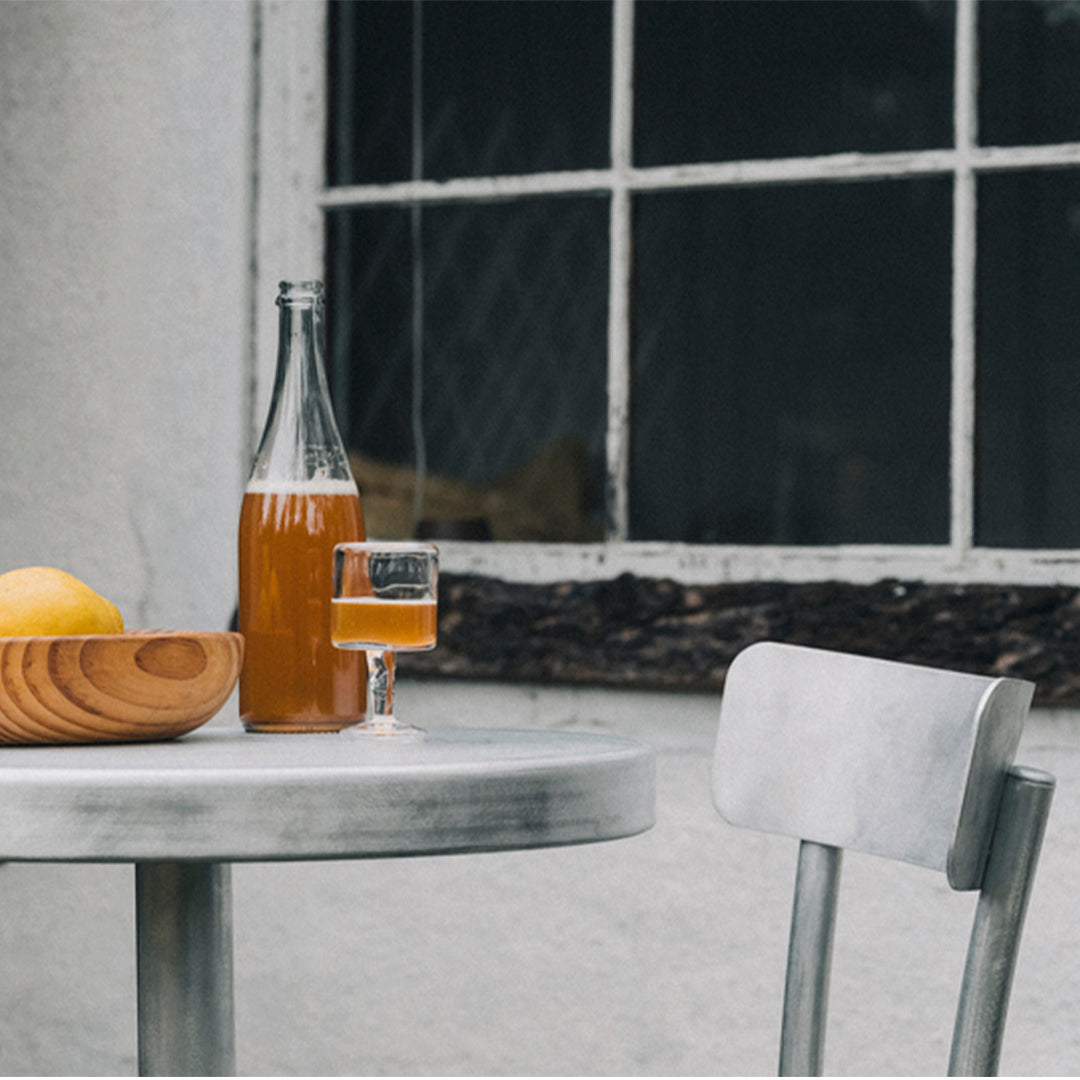 "Stylish gray table set with wooden bowl, yellow lemons, and amber drink in glass against a textured backdrop."