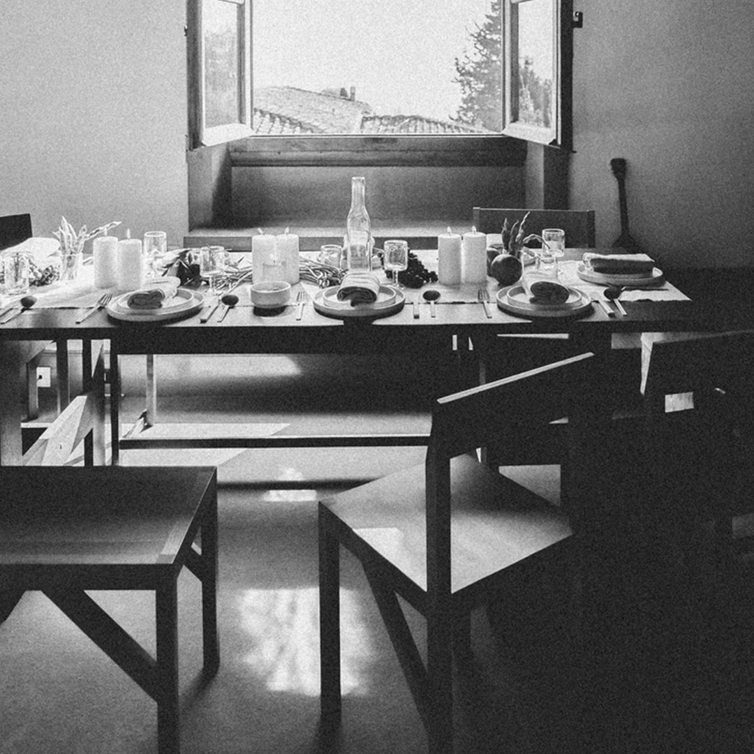 Elegant black and white dining scene with wooden chairs and a beautifully set table, featuring light and shadow contrasts.