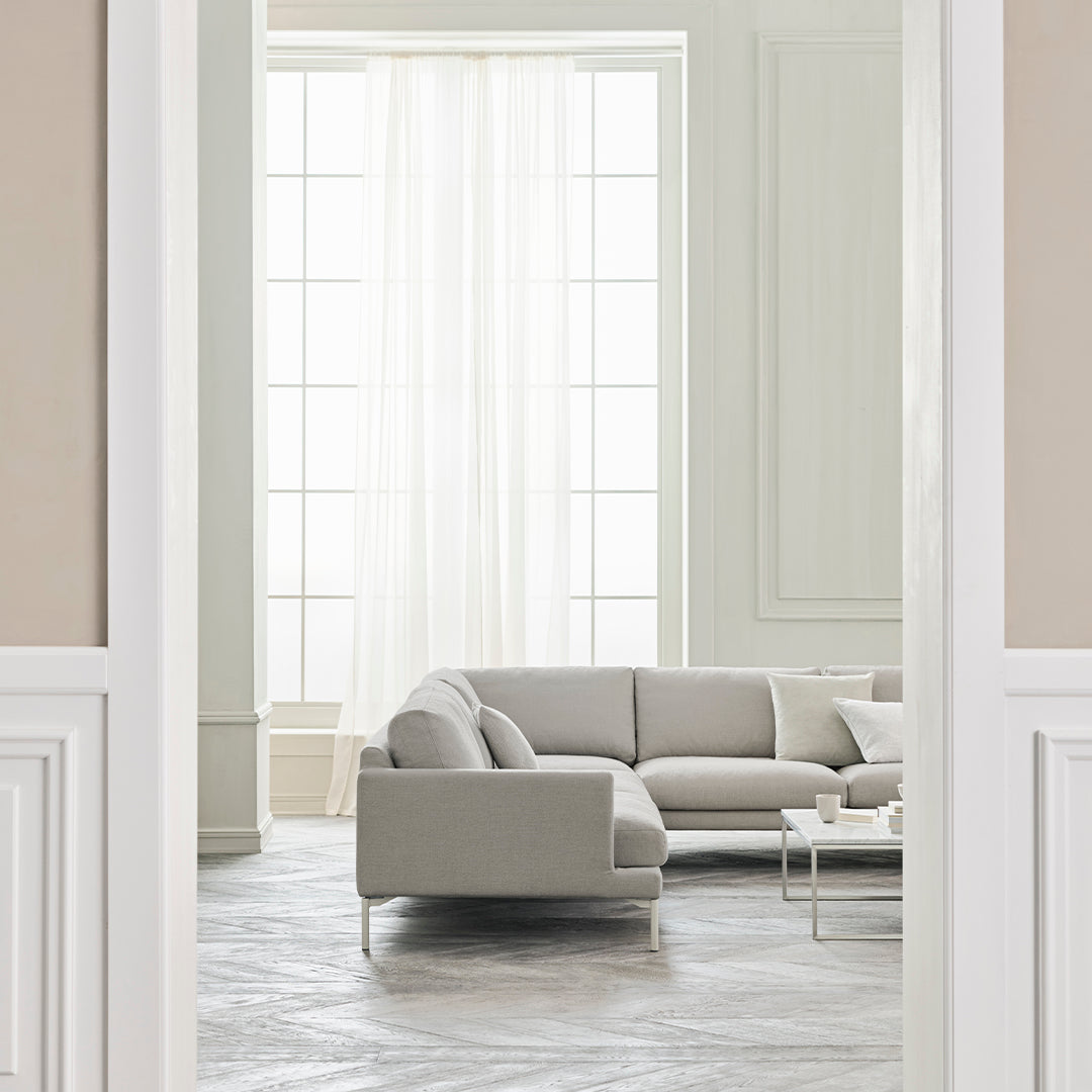 Light gray sectional sofa in a bright, airy room with neutral walls and patterned gray floor tiles.