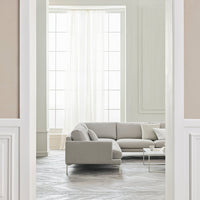 Light gray sectional sofa in a bright, airy room with neutral walls and patterned gray floor tiles.