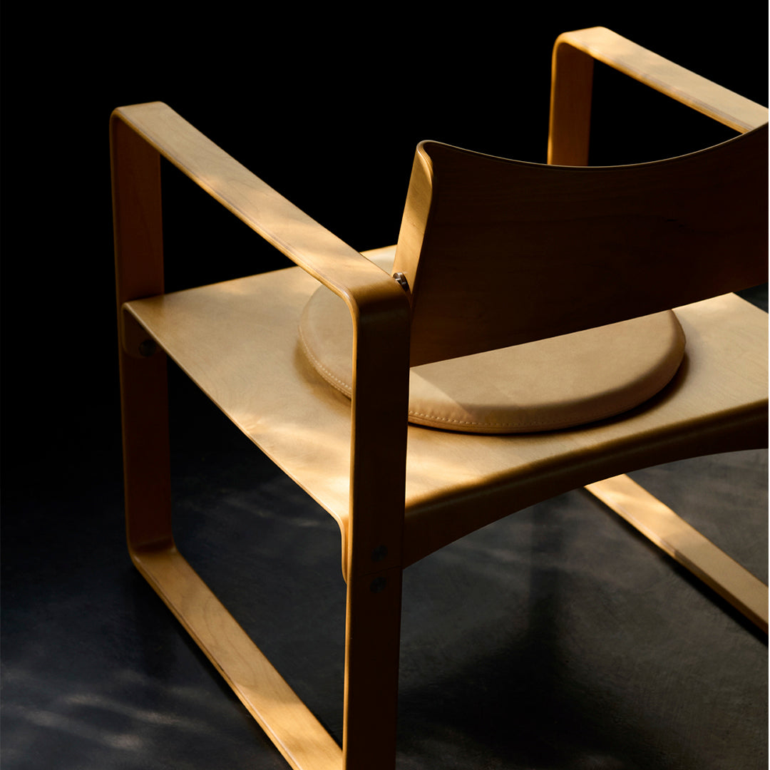 Light wood chair with a smooth, natural finish and minimalist design against a dark background.