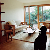 Cozy living room with natural wood tones, soft beige upholstery, and a light-colored rug against a green garden backdrop.