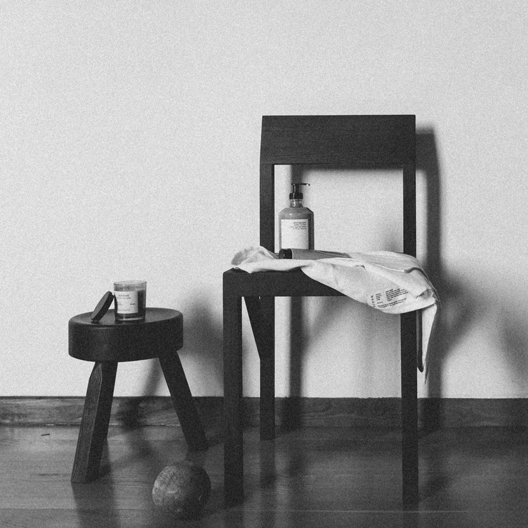 Black chair with a minimalistic design, accented by a patterned towel draped over it and a dark-stained stool nearby.