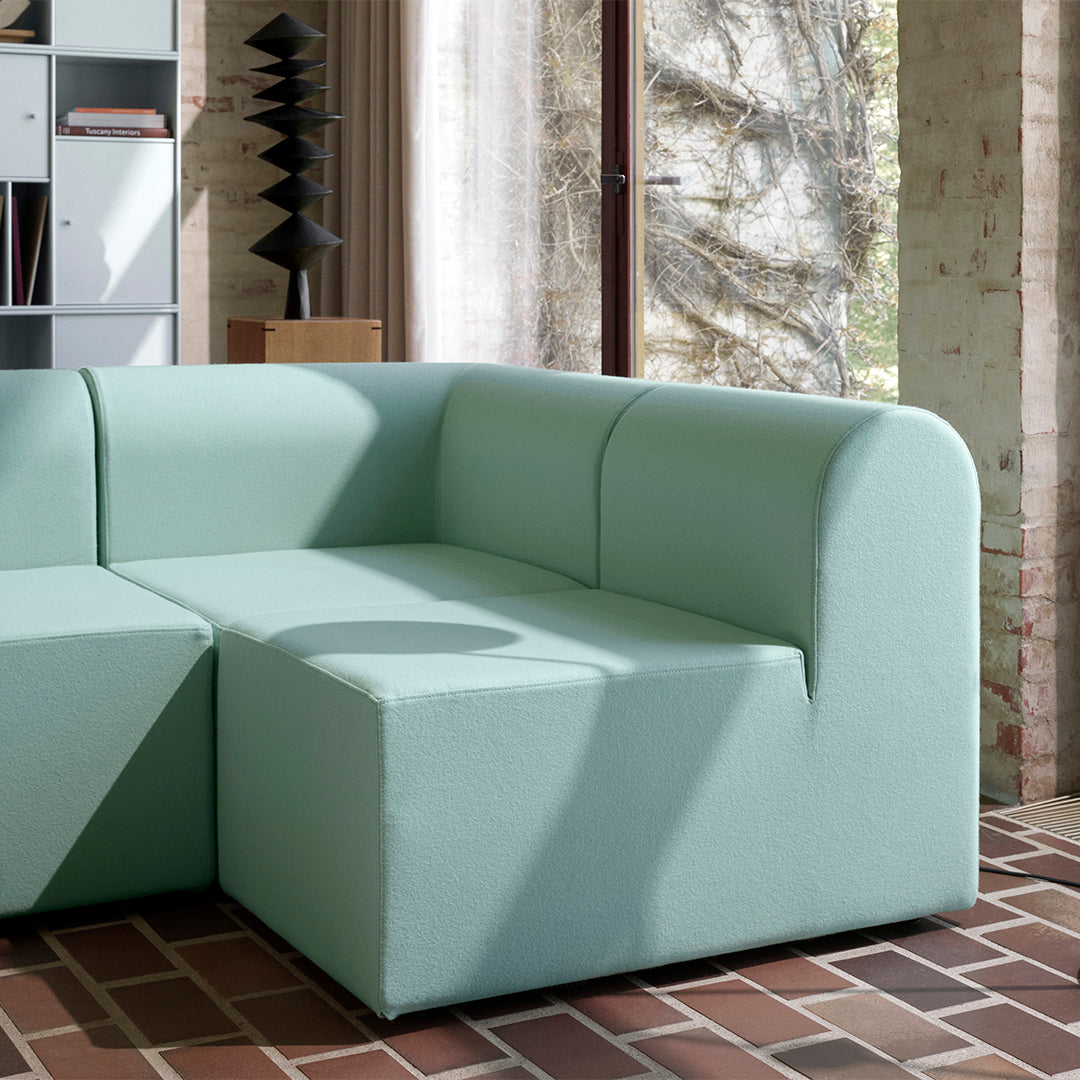 Mint green modular sofa with soft, rounded edges and a textured fabric against a brick floor.