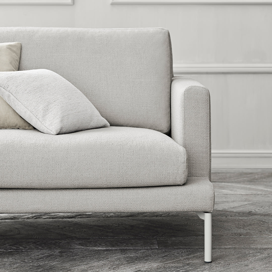 Light gray sofa with smooth fabric and subtle texture, accented by soft beige and white pillows. Modern minimalistic design.