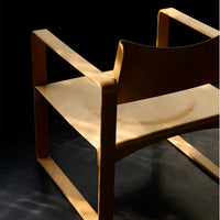Light wood chair with minimalistic design; smooth, natural finish; shadows create a subtle pattern against a dark background.