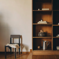 Minimalist black chair and wooden shelving unit with natural tones, showcasing neutral textiles and sleek metallic accents.
