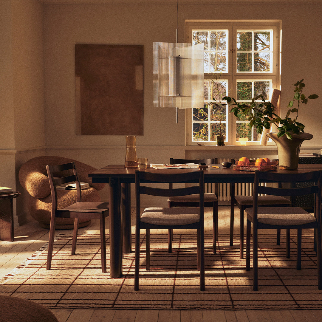 Elegant wooden dining table surrounded by neutral-toned chairs, with a striped beige rug and soft natural light.