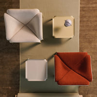 Overhead view of textured cushions in cream, light beige, white, and burnt orange, arranged on a soft green surface.