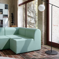 Mint green couch with soft curves, set against natural brick and wood textures, complemented by black accents.