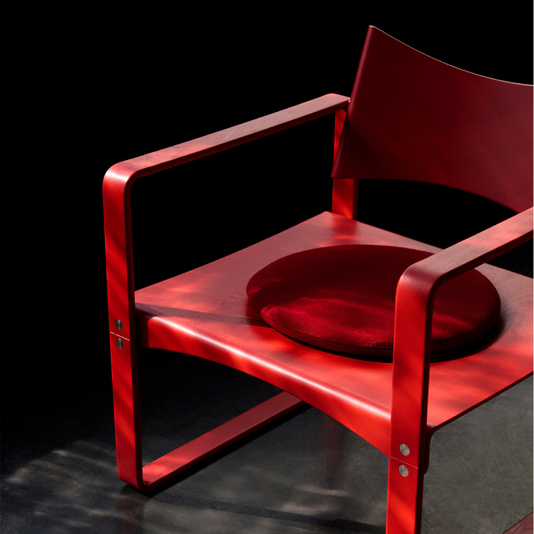 Bright red chair with a circular crimson cushion, set against a dark backdrop, showcasing sleek lines and modern design.