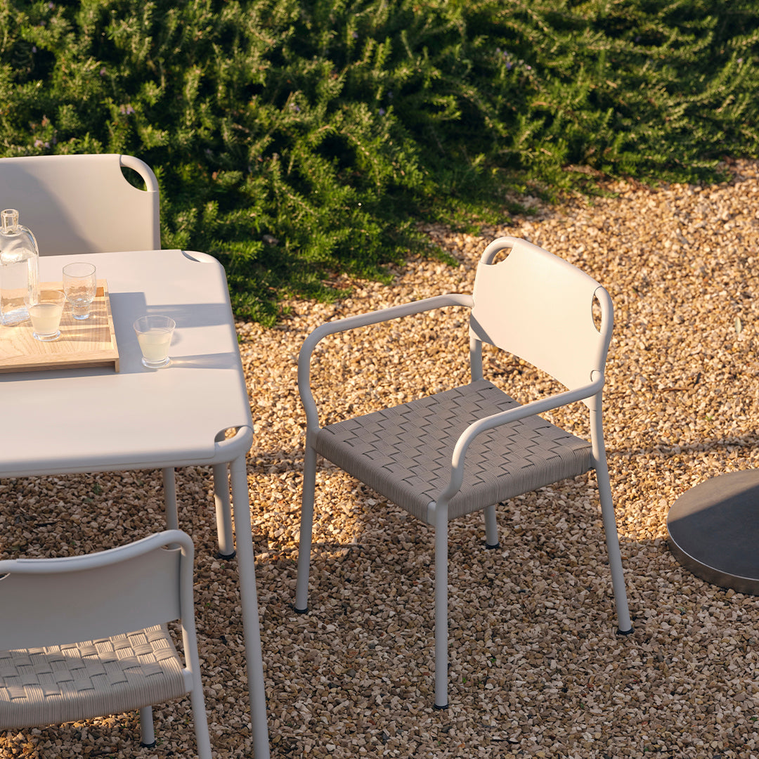 Light gray outdoor dining furniture set with a textured chair design, surrounded by natural greenery and gravel.