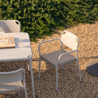 Light gray outdoor dining furniture set with a textured chair design, surrounded by natural greenery and gravel.