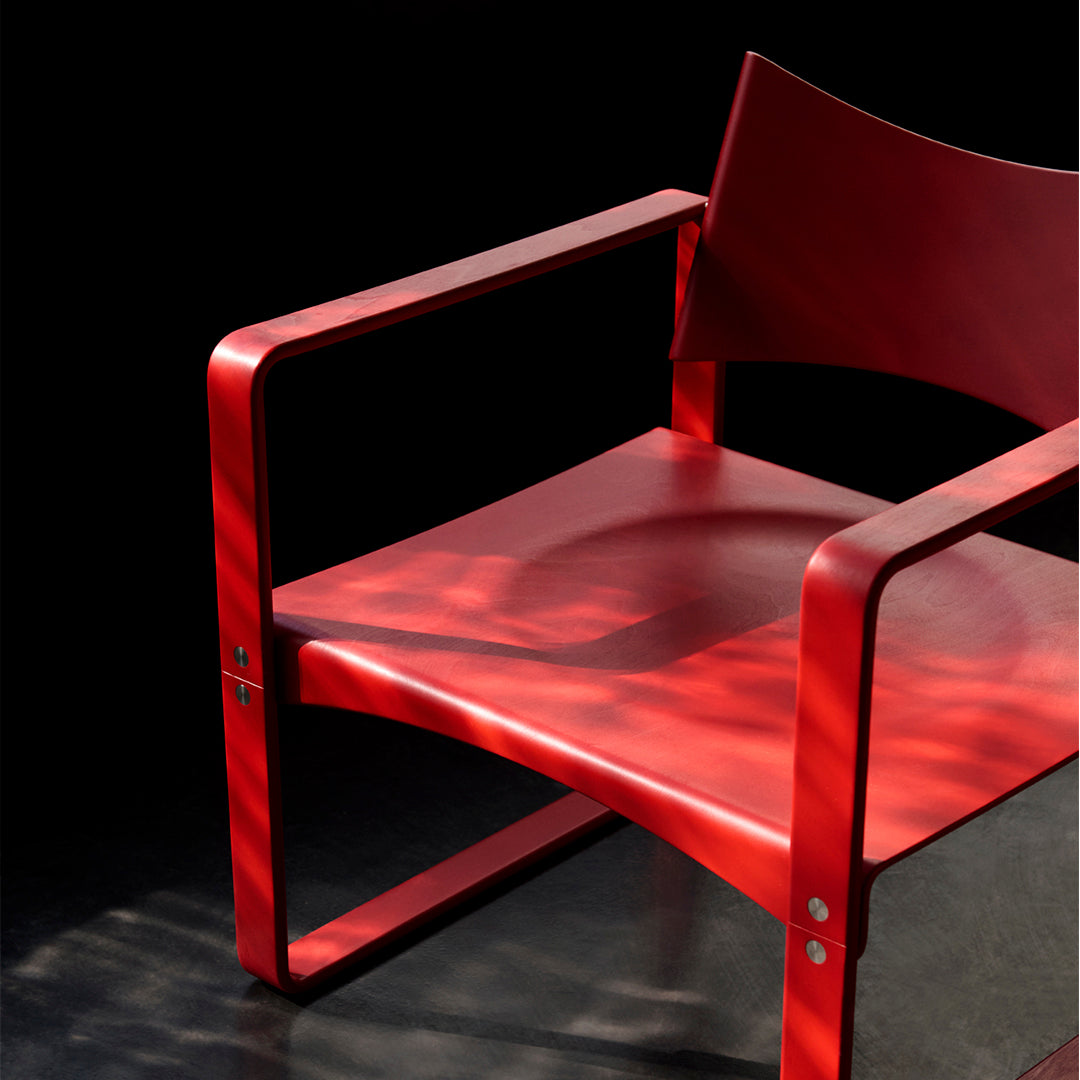 Red modern chair with sleek lines and minimalist design, against a dark background showcasing light reflections.