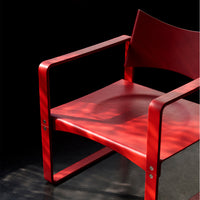 Red modern chair with sleek lines and minimalist design, against a dark background showcasing light reflections.