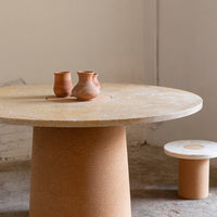Round beige table with smooth surface and earthy brown pottery on top, complementing a minimalist white stool.