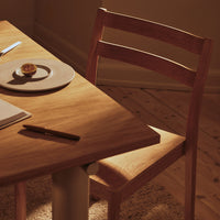Natural wood table with a warm, honey-toned finish and a minimalist design; simple, light brown chair beside a neutral plate.