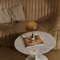 Beige quilted sofa with a round marble table, featuring a warm amber lamp and a creatively styled magazine.