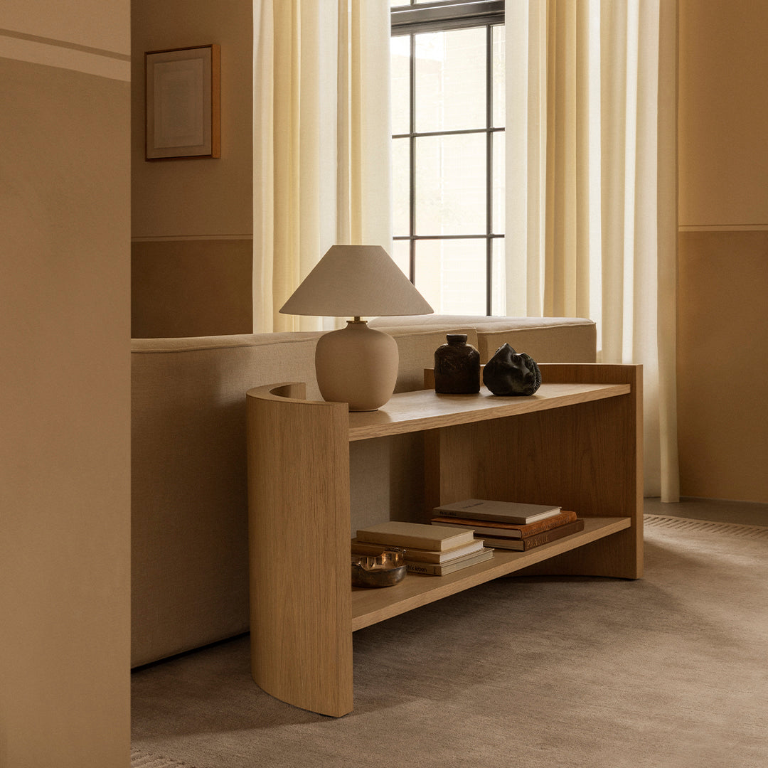 Light wood console table with smooth curves, neutral tones, and minimalistic decor against soft beige walls.