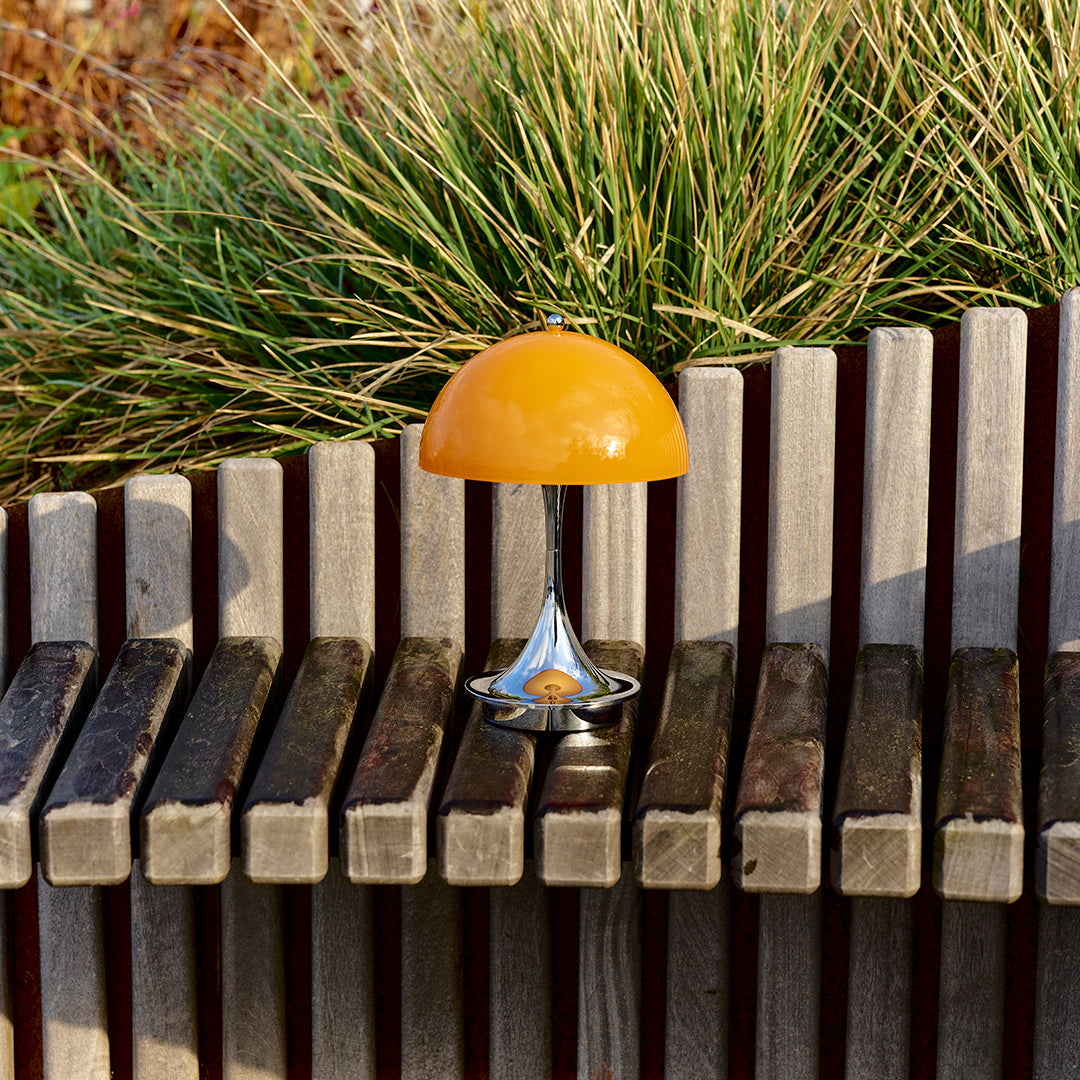 "Vibrant orange lamp with a sleek silver base, set against textured wooden slats and lush green grass."