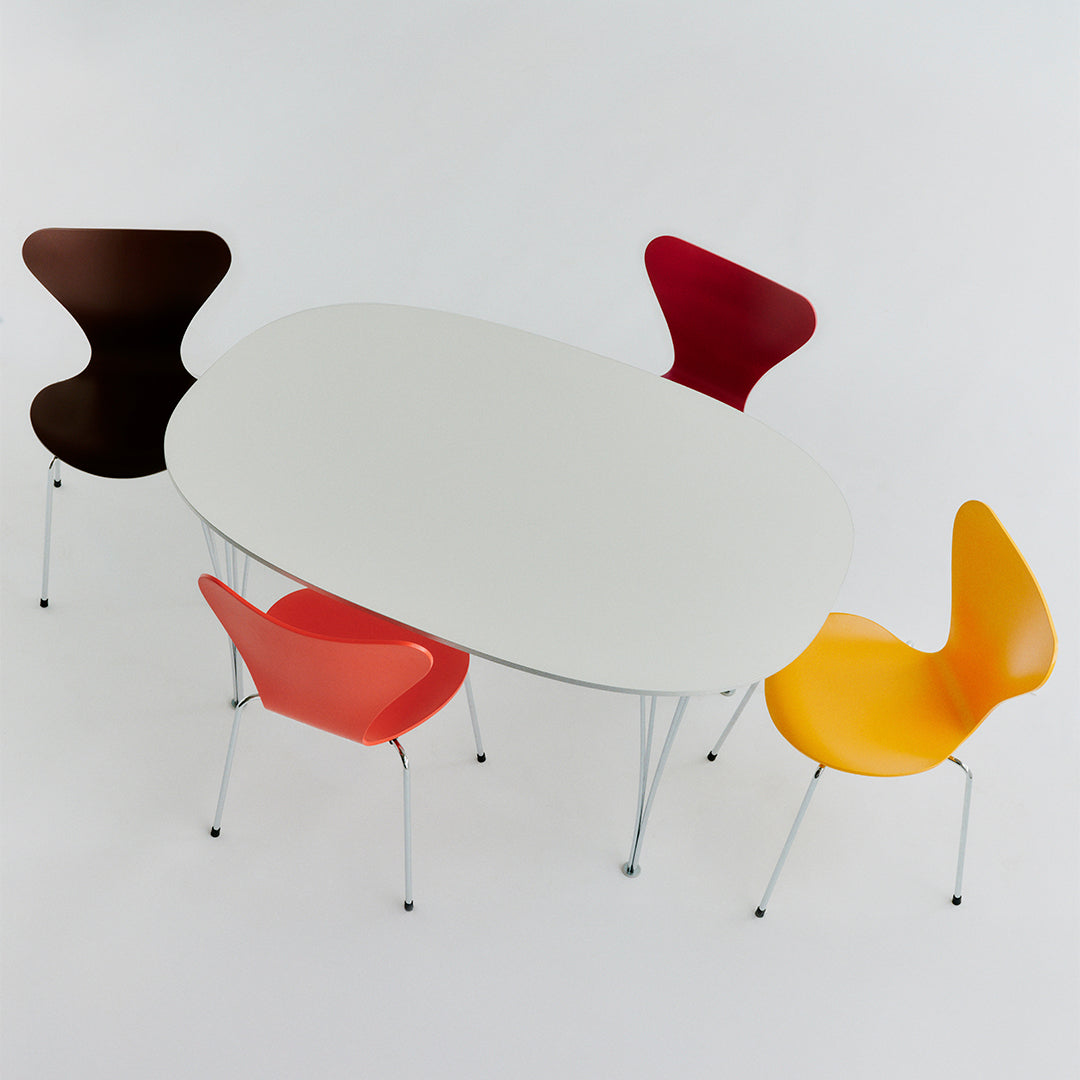 Modern oval dining table with a sleek white surface, surrounded by chairs in brown, red, and vibrant yellow.