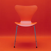 Vibrant orange chair against a solid orange backdrop, featuring a sleek design and chrome legs.