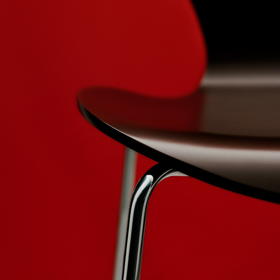 Glossy black chair seat with sleek chrome legs against a vibrant red backdrop. Modern minimalistic design.