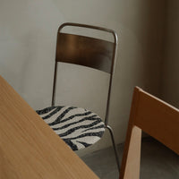 Zebra-patterned chair cushion in black and white with a sleek silver metal frame, set against a minimalist backdrop.