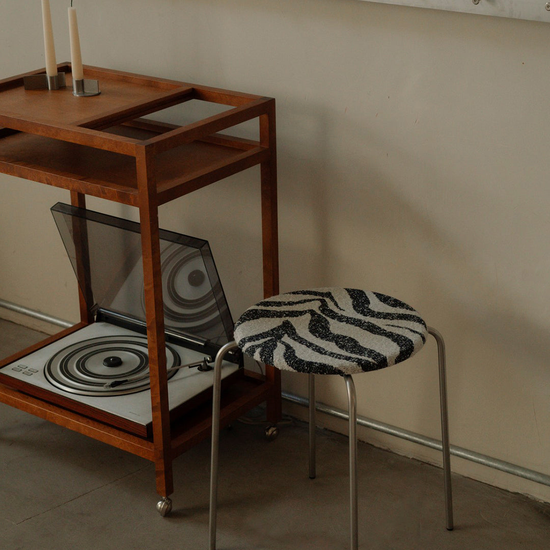 "Stylish stool with a black and white wavy pattern, complementing a wooden cart and circular accents."