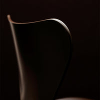 Sleek dark brown chair silhouette with smooth curves against a deep black background, emphasizing elegant design.