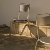 Minimalist metal chairs in silver finish, set against a neutral stone background with soft, natural lighting.