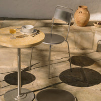 "Round stone-patterned table with silver chair and shadows, set against a natural stone floor and clay pottery."