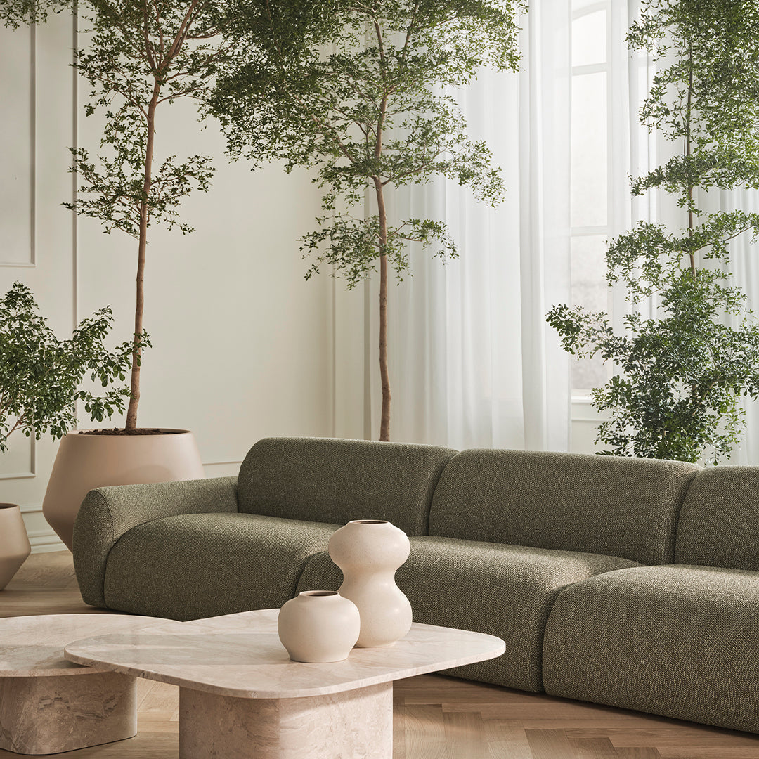 Sleek green sofa with textured fabric, complemented by beige ceramic vases and marble coffee table in a serene setting.