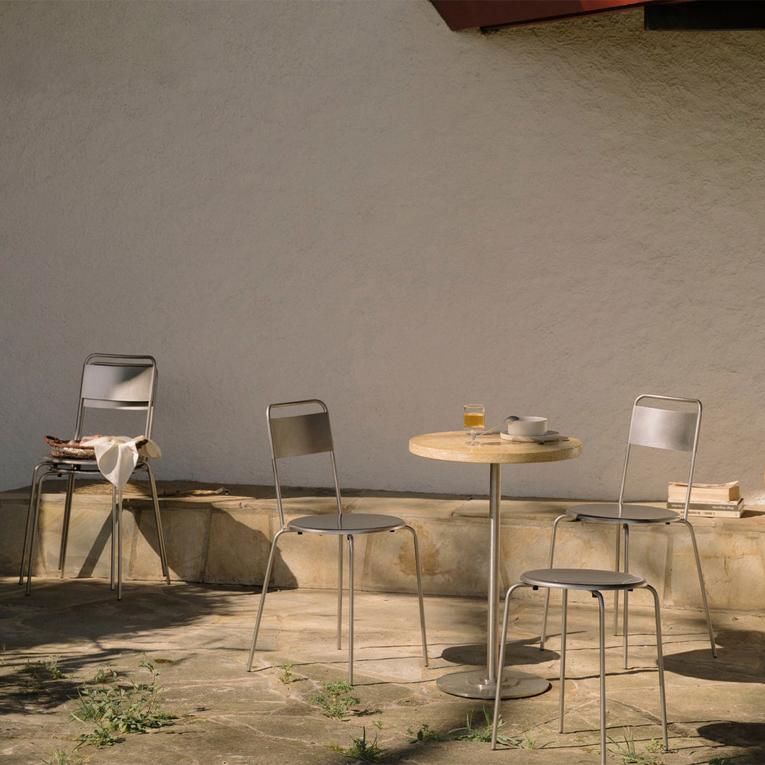"Minimalist outdoor cafe set with gray chairs and a round wooden table, set against a neutral wall background."