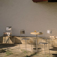"Minimalist outdoor cafe set with gray chairs and a round wooden table, set against a neutral wall background."