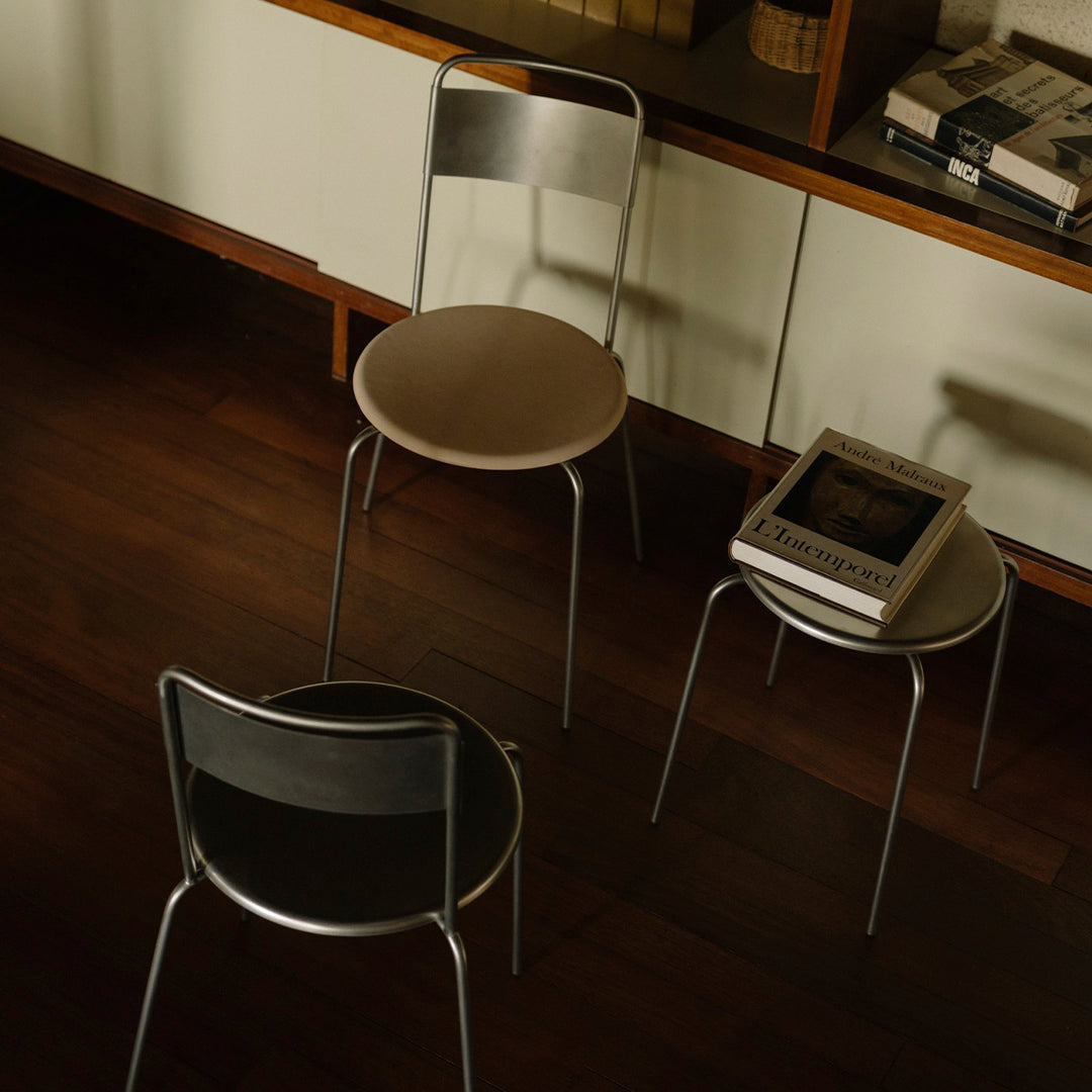 Set of three modern chairs featuring black, beige, and metallic finishes on a dark wooden floor. Minimalist design.