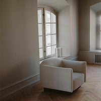 Soft beige armchair with a textured fabric, set against a neutral-toned wall and light wooden floor.
