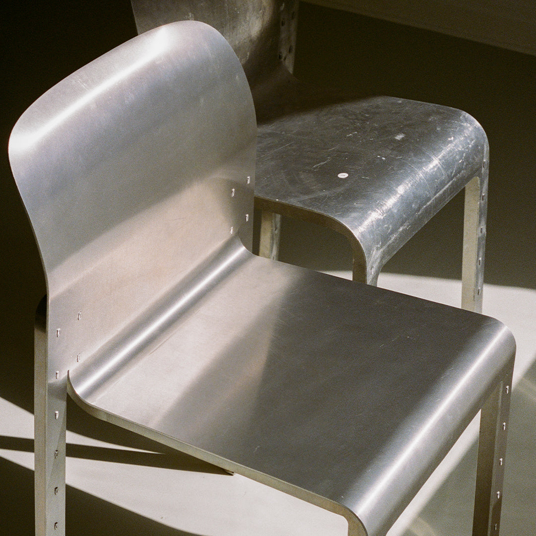 Sleek aluminum chairs with a brushed metallic finish, featuring minimalistic design and smooth contours.