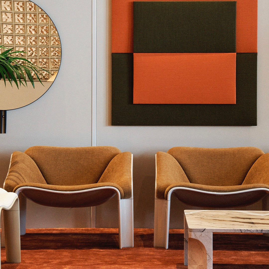 Two modern chairs in warm brown with beige and orange accents, set against a geometric mural of earthy tones.