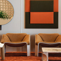 Two modern chairs in warm brown with beige and orange accents, set against a geometric mural of earthy tones.