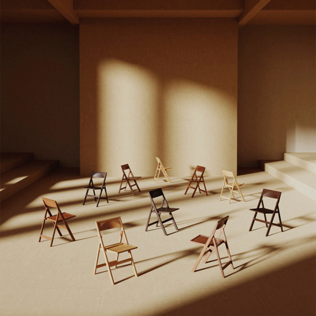 Assorted folding chairs in natural wood tones and dark finishes arranged in a sunlit, minimalistic setting.