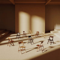 Assorted folding chairs in natural wood tones and dark finishes arranged in a sunlit, minimalistic setting.