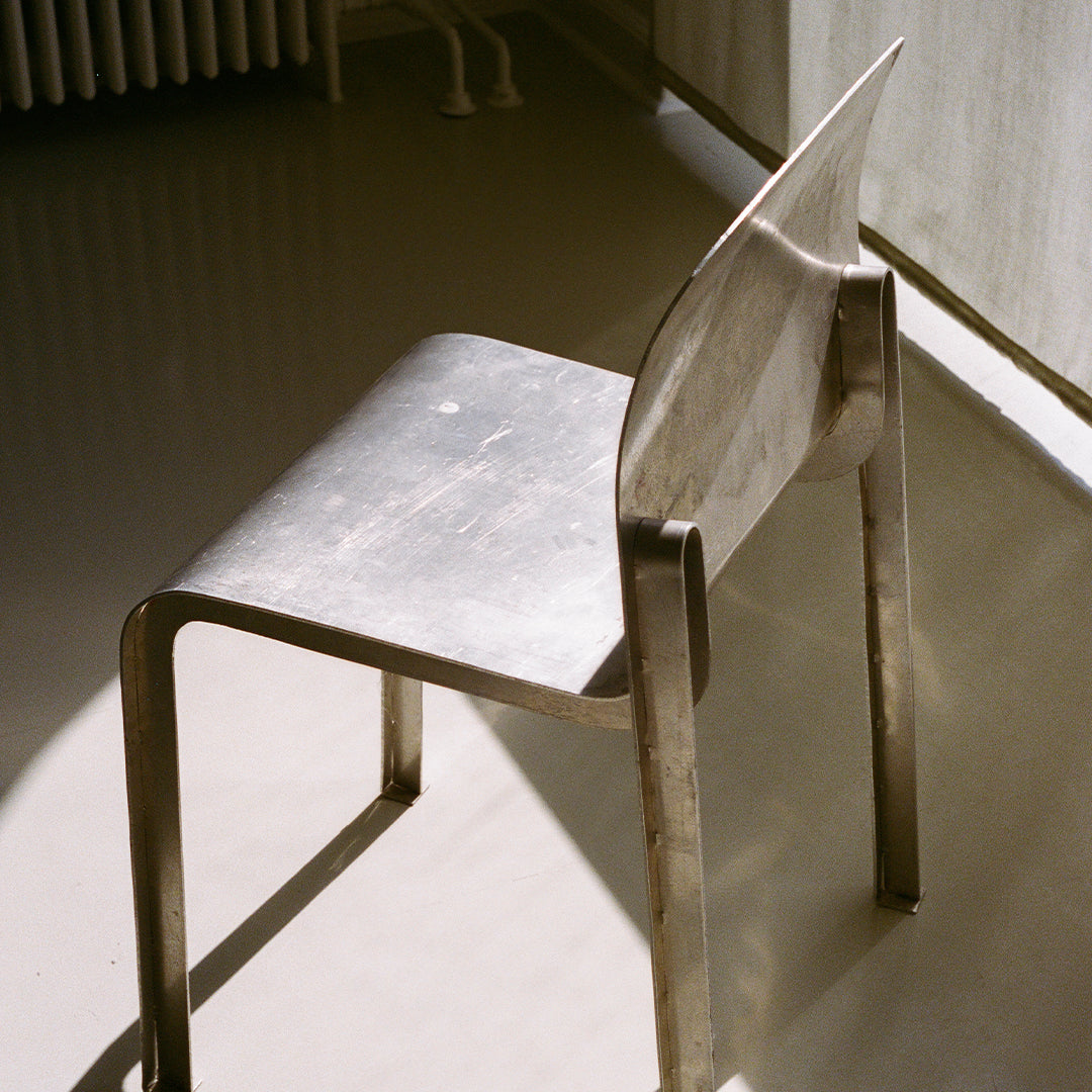 Sleek silver metal chair with smooth, minimalist design and subtle reflections in natural light.